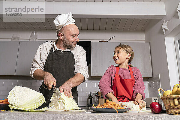 Vater und Tochter tragen Schürzen und bereiten zu Hause in der Küche gesunde Mahlzeiten zu