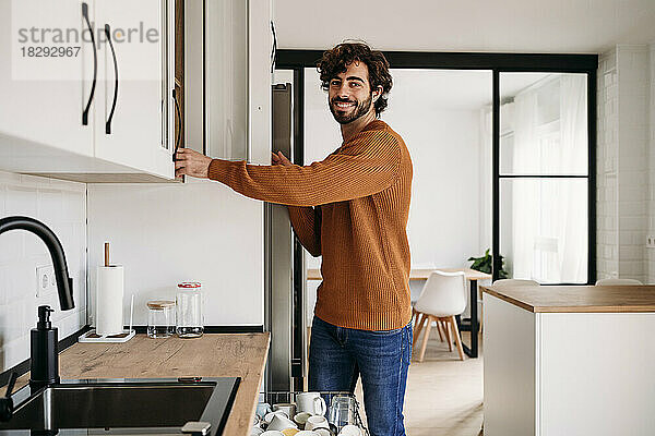Happy man opening cabinet in kitchen at home