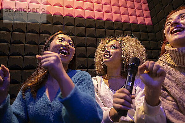 Happy friends enjoying holding microphone at amusement arcade