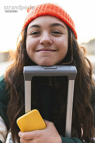 Lächelndes Mädchen lehnt Gesicht an Koffergriff