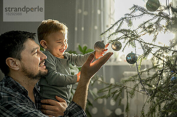 Glücklicher Vater und Sohn schmücken zu Hause den Weihnachtsbaum