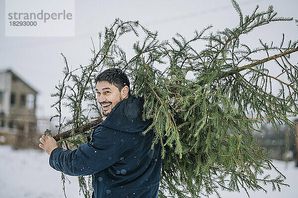 Glücklicher Mann trägt Tannenbaum im Schnee