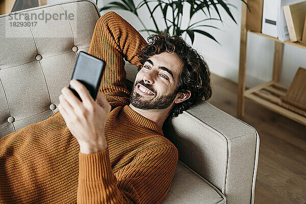 Glücklicher junger Mann  der sein Smartphone auf dem Sofa benutzt