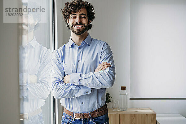 Happy businessman standing with arms crossed in office
