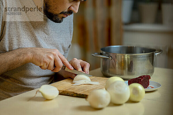 Mann schneidet weiße Zwiebeln auf Schneidebrett in der Küche