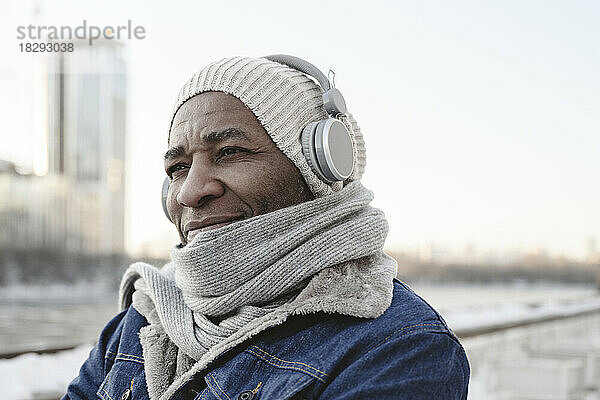 Lächelnder Mann in warmer Kleidung  der Musik über kabellose Kopfhörer genießt