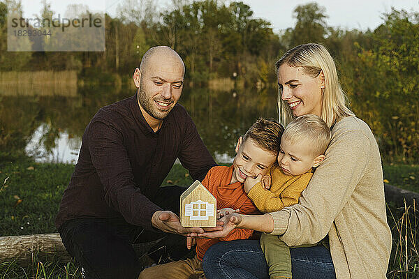 Lächelnde Eltern mit Kindern halten ein Holzmodellhaus in der Natur