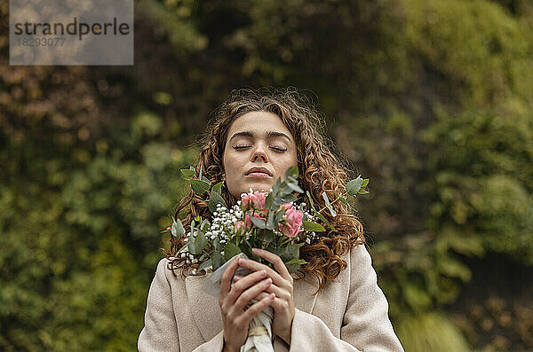 Junge Frau mit geschlossenen Augen hält einen Blumenstrauß in der Hand