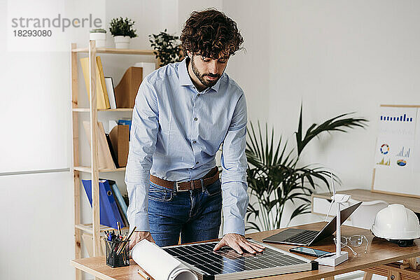 Junger Geschäftsmann schaut am Schreibtisch im Büro auf Solarpanel