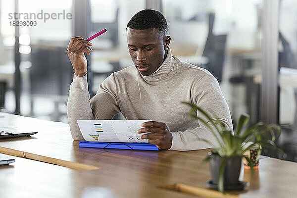 Junger Geschäftsmann prüft Dokument am Schreibtisch im Büro
