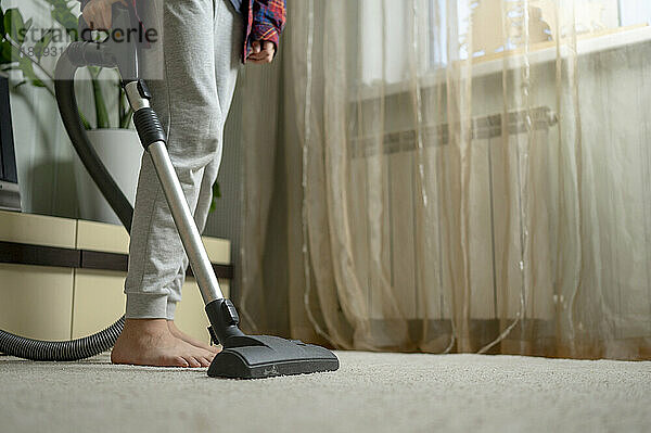 Hand eines Jungen  der zu Hause einen Staubsauger verwendet  um den Teppich zu reinigen