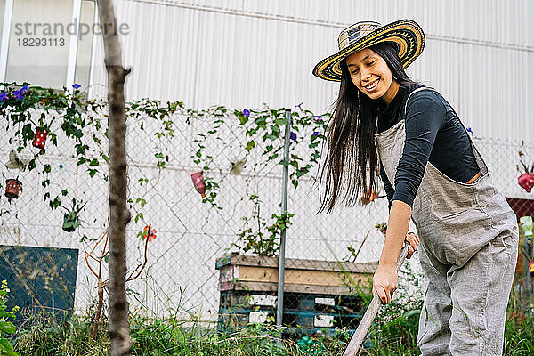Glückliche Frau bei der Gartenarbeit mit Rechen im städtischen Garten