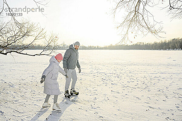 Vater und Tochter laufen im Winter Eislaufen auf dem zugefrorenen See
