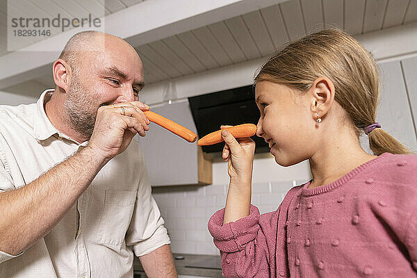 Vater und Tochter amüsieren sich zu Hause mit Karotten in der Küche