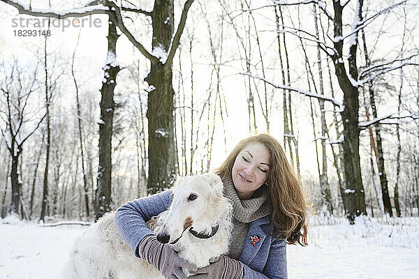 Lächelnde reife Frau umarmt Windhund im Winterpark