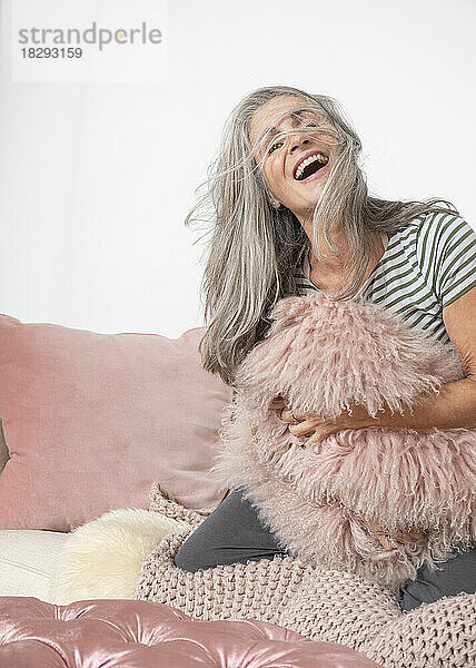 Happy mature woman having fun with cushions at home