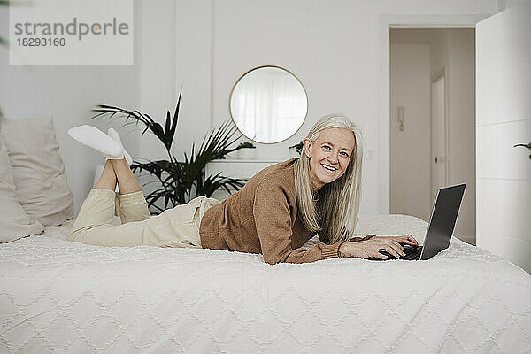 Glückliche Frau  die zu Hause mit Laptop im Bett liegt