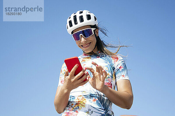 Glücklicher Radfahrer  der sein Smartphone unter Himmel benutzt