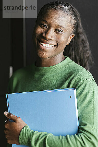 Smiling businesswoman holding file folder in front of wall
