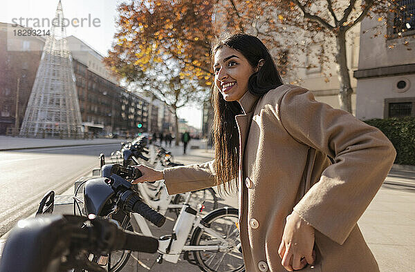 Glückliche junge Frau  die an einem sonnigen Tag ein Fahrrad mietet