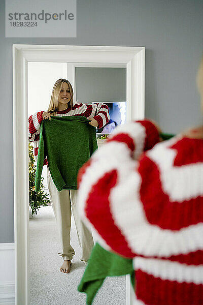 Glückliches Mädchen  das zu Hause vor dem Spiegel einen grünen Pullover probiert