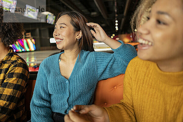 Happy young friends sitting on sofa at bowling alley