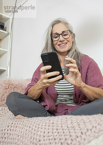 Glückliche Frau  die zu Hause auf dem Sofa sitzt und ihr Mobiltelefon benutzt