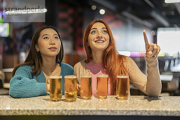 Glückliche Frau zeigt auf einen Freund mit Gläsern Bier am Tresen