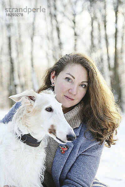 Reife Frau mit weißem Windhund im Winterpark