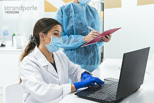 Zahnarzt arbeitet am Laptop mit Kollege und prüft Dokumente am Schreibtisch in der Klinik