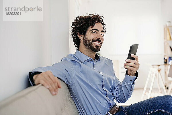 Lächelnder Geschäftsmann sitzt mit Smartphone im Büro