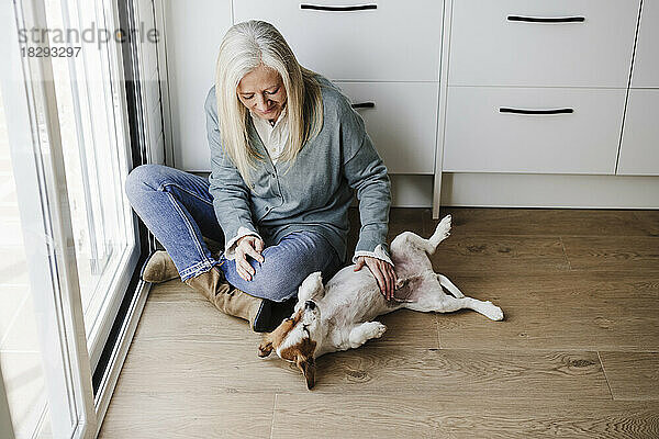 Reife Frau streichelt Hund auf dem Boden zu Hause