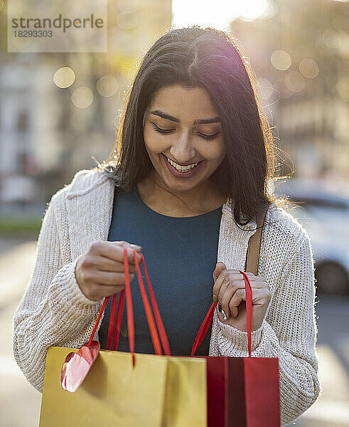 Lächelnde junge Frau schaut an einem sonnigen Tag in Einkaufstüten