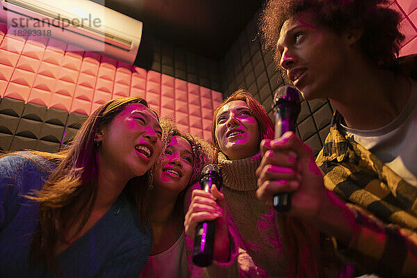 Gemischtrassige Freunde singen Karaoke über Mikrofone in einer Spielhalle