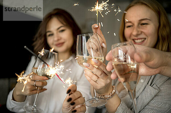 Glückliche Freunde  die zu Hause mit Gläsern Champagner und Wunderkerzen feiern