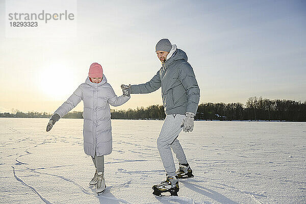 Glückliches Mädchen mit Vater beim Eislaufen auf dem Wintersee