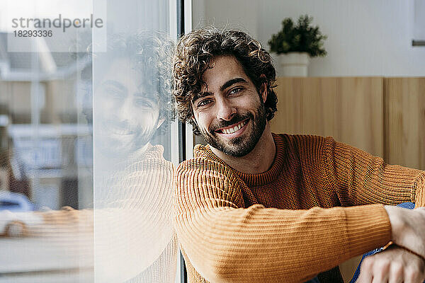 Happy man leaning on glass window at home