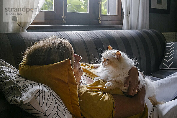 Ältere Frau kuschelt zu Hause mit Katze auf dem Sofa