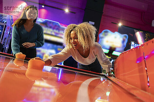 Happy women enjoying playing air hockey at amusement arcade