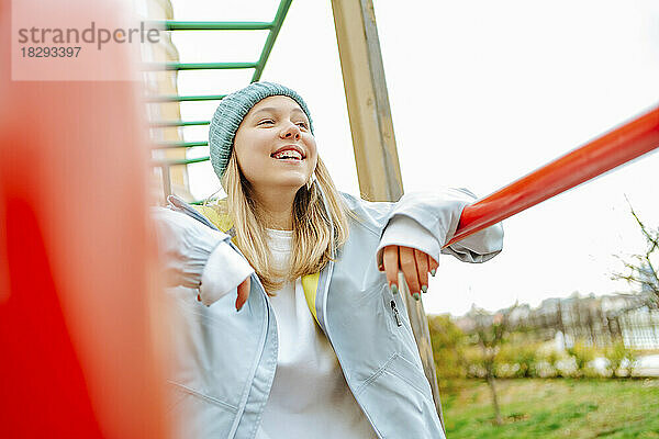 Fröhliches Teenager-Mädchen mit Strickmütze steht auf dem Spielplatz