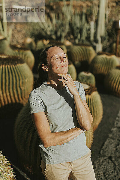 Lächelnde Frau mit geschlossenen Augen steht im Kaktusgarten