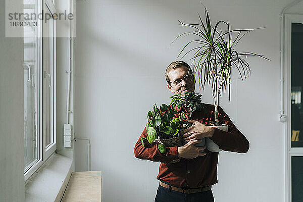 Lächelnder Geschäftsmann steht mit Pflanzen vor der Wand