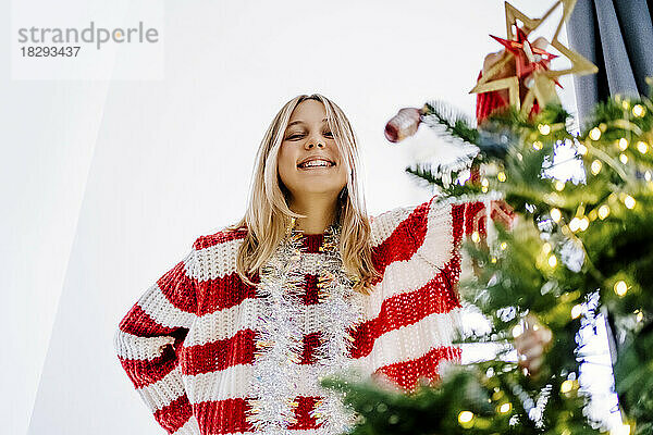 Glückliches Mädchen mit Lametta  das zu Hause am Weihnachtsbaum steht