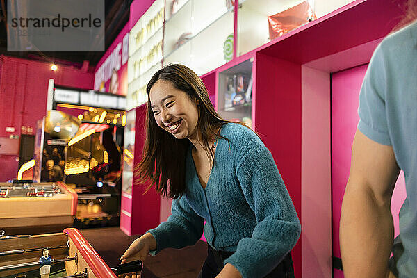 Happy young woman playing table soccer at arcade
