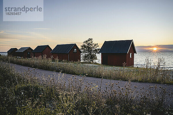 Schweden  Öland  Byxelkrok  Fußweg  der sich bei Sonnenuntergang hinter Fischerhütten an der Küste erstreckt