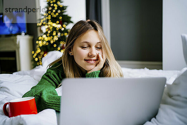 Lächelndes Mädchen  das sich einen Film auf dem Laptop ansieht und zu Hause im Bett liegt
