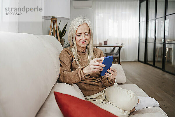 Glückliche reife Frau  die ihr Smartphone auf dem Sofa benutzt