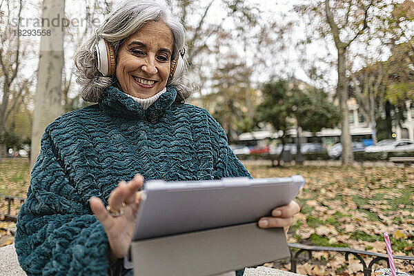 Glückliche ältere Frau sitzt im Park und benutzt einen Tablet-PC