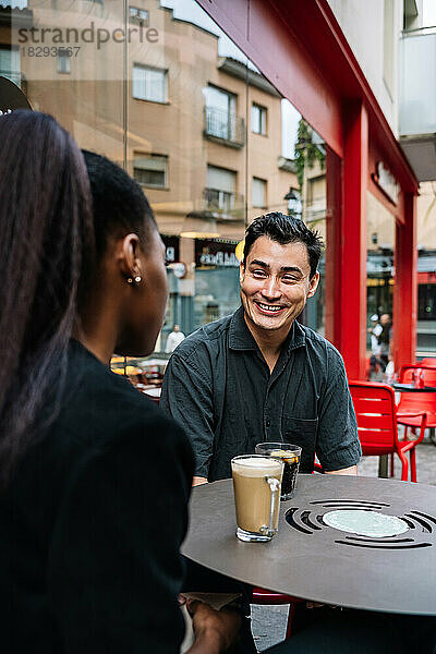 Lächelnder Geschäftsmann im Gespräch mit Kollegen im Straßencafé