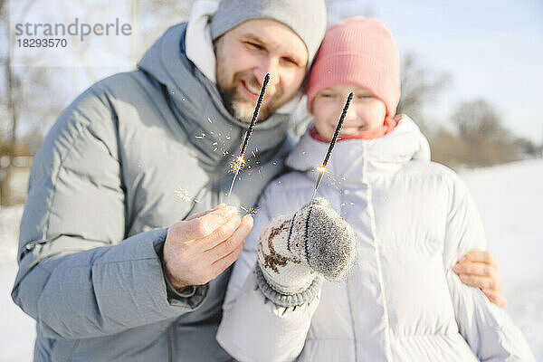 Glücklicher Vater und Tochter halten Wunderkerzen im Winter